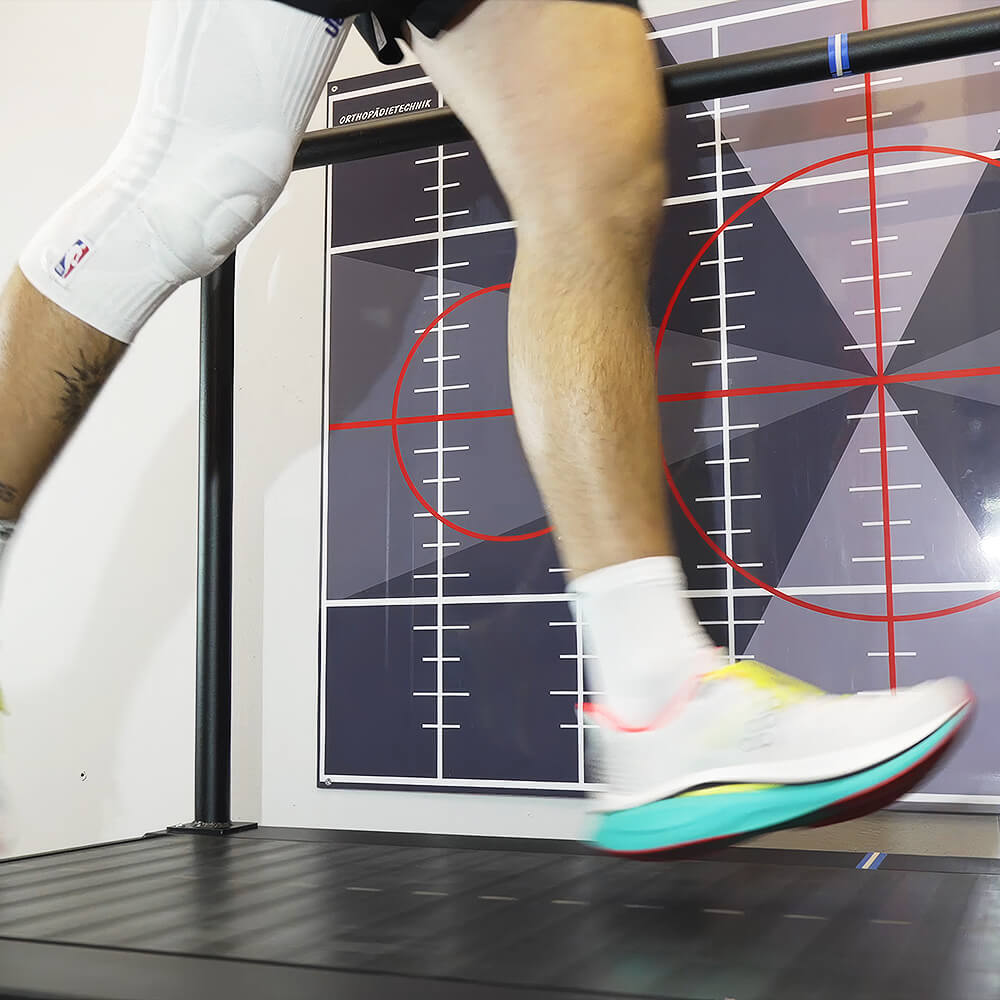 Detailaufnahme eines Fußes in Laufschuhen auf dem Laufband, im Hintergrund eine Messwand zur Analyse der Laufbewegung